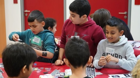 Ein Kind hält eine Flüssigkleber-Packung in der Hand während einer Bastel-Aktion der Kindervesperkirche 2023. Mit der Aktion will sich die Evangelische Kirche für Nächstenliebe einsetzen.