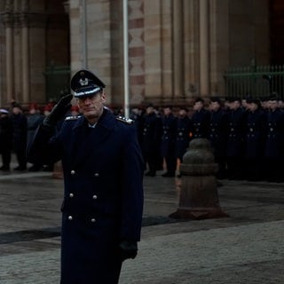 Ein Bundeswehrsoldat beim Gelöbnis vor dem Speyerer Dom salutiert. Im Hintergrund stehen zahlreiche Rekruten.