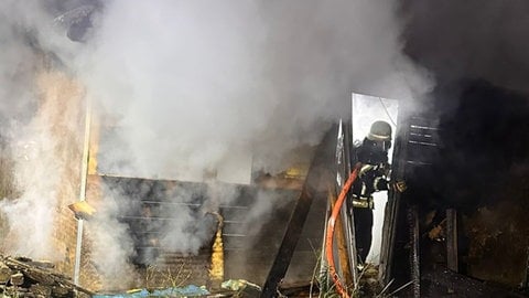 Hohe Flammen schlagen aus einer Kleingartenanlage am Flughafen Speyer. Feuerwehrmänner bekämpfen die Flammen.