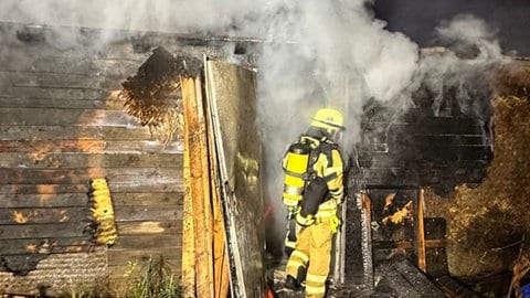 Ein Feuerwehrmann bekämpft den Brand einer Gartenlaube am Flughafen Speyer.