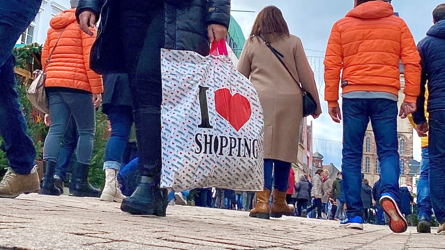 Menschen laufen mit Taschen und Tüten durch die Fußgängerzone in Speyer mit dem Dom im Hintergrund.