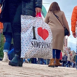 Menschen laufen mit Taschen und Tüten durch die Fußgängerzone in Speyer mit dem Dom im Hintergrund. 