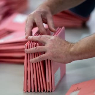 Hände sortieren Briefwahlunterlagen. Symbolbild. Wegen der vorgezogenen Bundestagswahl muss bei der Briefwahl alles ganz schnell gehen. Maikammer will die Unterlagen von Boten verteilen lassen.