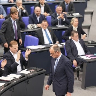 Friedrich Merz, CDU-Bundesvorsitzender und CDUCSU-Fraktionsvorsitzender im Bundestag, läuft an der AfD-Fraktion (rechts) vorbei, die nach der Bekanntgabe der Ergebnisse der Abstimmung für eine Verschärfung der Migrationspolitik reagiert.