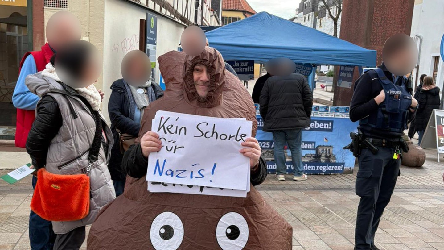 Mann protestiert in Neustadt in einem Kostüm, das wie ein Kackhaufen aussieht