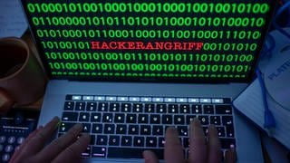 Zwischen dem Binärcode auf einem Laptopmonitor ist das Wort Hackerangriff zu sehen. 
