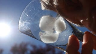  Eine Frau kühlt ihre Stirn mit einem Glas mit Eiswürfel.