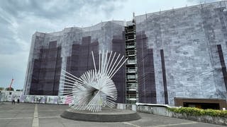Die graue Fassade des Mainzer Rathauses ist im August 2022 von Baugerüsten umstellt und mit einem Banner verhängt