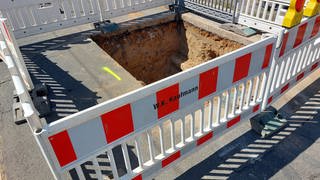 In der Elbestraße in Mainz-Gonsenheim ist ein Loch in der Straße, das von Baustellenzäunen abgesperrt ist