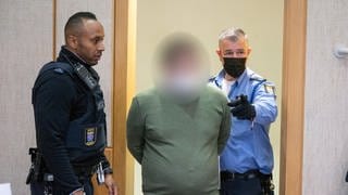 Mitarbeiter der Justiz führen den Angeklagten in den Verhandlungssaal des Landgerichts in Frankfurt. Der 35-Jährige Angeklagte soll als Fußball-Jugendtrainer in zahlreichen Fällen Jugendliche vergewaltigt und missbraucht haben.