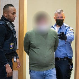 Mitarbeiter der Justiz führen den Angeklagten in den Verhandlungssaal des Landgerichts in Frankfurt. Der 35-Jährige Angeklagte soll als Fußball-Jugendtrainer in zahlreichen Fällen Jugendliche vergewaltigt und missbraucht haben.