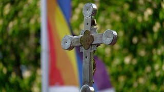 Ein Kreuz steht vor einer Regenbogenflagge. Im Bistum Mainz wird am Sonntag ein Gottesdienst zur Beauftragung der queersensibler Pastoral gefeiert.