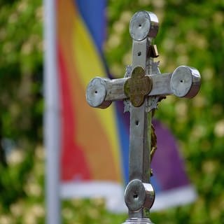 Ein Kreuz steht vor einer Regenbogenflagge. Im Bistum Mainz wird am Sonntag ein Gottesdienst zur Beauftragung der queersensibler Pastoral gefeiert.