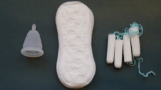 Eine Menstruationstasse, Slipeinlagen und Tampons verschiedener Hersteller liegen auf einem Tisch. Die Stadt Mainz will Periodenprodukte künftig kostenlos anbieten.