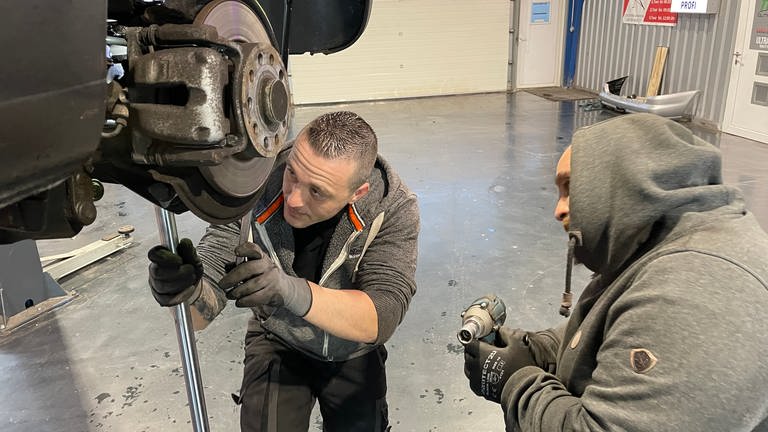 Zwei Männer schrauben an einem Auto. Manuel Saba betreibt in Gau-Algesheim eine Hobby-Werkstatt, wo Menschen ihr Auto selbst reparieren können.