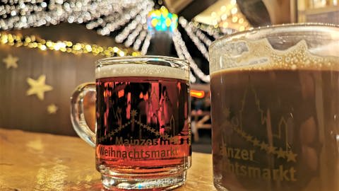 Auf einem Stehtisch auf dem Mainzer Weihnachtsmarkt steht ein Glas mit Glühwein und ein Glas mit heißer Schokolade.