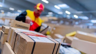 Ein Paketzusteller sortiert und räumt in einer Zustellbasis von Deutsche Post DHL Pakete in ein Zustellfahrzeug.