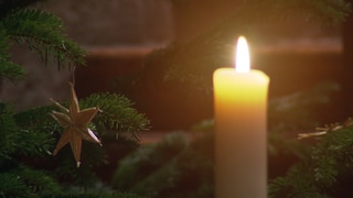 Eine leuchtende Kerze vor einem mit einem Strohstern geschmückten Weihnachtesbaum im Hohen Dom zu Mainz