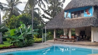 Das Haus, das die Gemeinde Wöllstein in Kenia geerbt hat, hat ein Reetdach. Im Giebel an der Hauswand wurden zwei Greifvögel aufgemalt. Vor dem Haus gibt es einen Pool. 