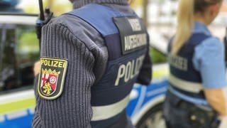Zwei Polizisten in Uniform stehen in Mainz vor einem Polizeiauto.