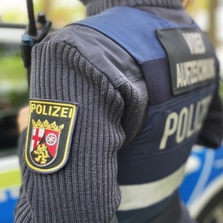 Zwei Polizisten in Uniform stehen in Mainz vor einem Polizeiauto.