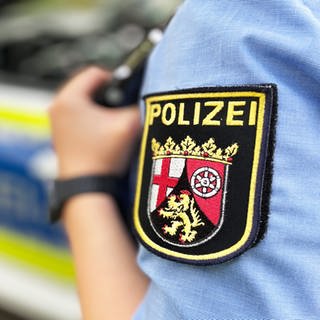 Eine Polizistin steht neben einem Polizeiauto. Auf dem Oberarm ist das Wappen vom Land Rheinland-Pfalz zu sehen.