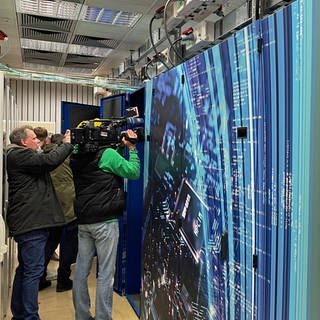 In Mainz wurde der neue Hochleistungsrechner Mogon eingeweiht. Der Rechner sieht unspektakulär aus - wie eine große Schrankwand. Journalisten versuchen mit ihren Kameras dennoch ein ansprechendes Bild zu machen. 