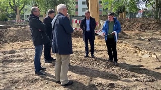 Männer stehen auf einer Baustelle. Günter Brücken von der Landesarchäologie RLP informiert über archäologische Funde in Alzey.