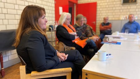 Manuela Matz sitzt auf einem Stuhl an einem Tisch bei einem Treffen mit dem Mainzer Flüchtlingsrat.
