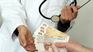 Ein Arzt hält die Hand auf und bekommt mehrere Euro Scheine gereicht.