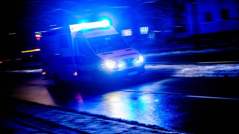 Ein Rettungswagen fährt nachts mit eingeschaltetem Blaulicht durch eine Straße.