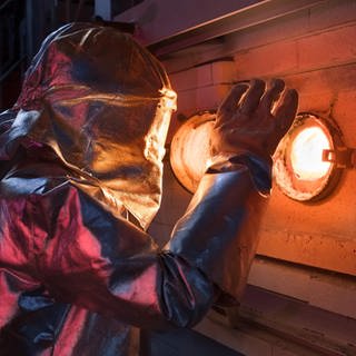 Ein Schott-Mitarbeiter steht im Hitzeschutzanzug vor einem Schmelzofen
