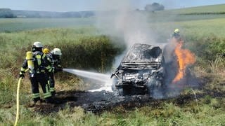 letzte Löscharbeiten an einem völlig ausgebranntes Auto in einem Feld bei Hargesheim