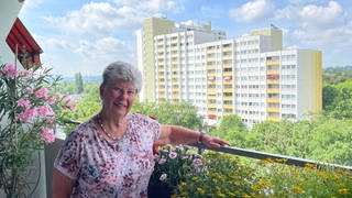 Edith Dolezik steht zwischen Blumen auf dem Balkon ihrer Wohnung im Hochhaus an der Elsa-Brändström-Straße in Mainz-Gonsenheim, wo sie seit 50 Jahren lebt. Im Hintergrund ein weiteres Hochhaus