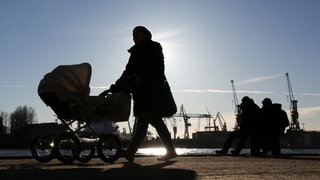 Eine junge Frau mit Kinderwagen geht im Gegenlicht der Sonne. Das Foto ist ein Symbolbild.