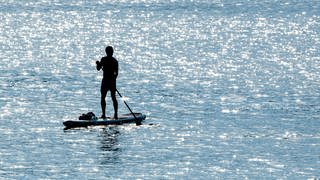 Mann steht auf Stand-Up-Paddle-Board auf dem Wasser