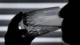 Ein Mann trinkt ein Glas Wasser. Das Hitzetelefon von Worms erinnert Senioren daran, genug zu trinken