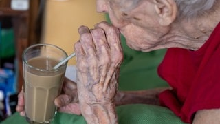 Eine Seniorin trinkt aus einem Glas mit einem Strohhalm kalten Kaffee. Vom Wormser Hitzetelefon wird sie daran erinnert, genug zu trinken