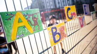 Bei der Einschulungsfeier einer Grundschule hängen am Zaun Zettel mit dem Alphabet. In Worms kritisiert ein Flüchtlingsverein, dass Kinder an Wormser Grundschulen zu wenig Deutsch lernen. 