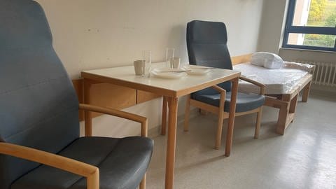 Ein Krankenhauszimmer mit blauen Stühlen und einem Tisch im ehemaligen Ingelheimer Krankenhaus