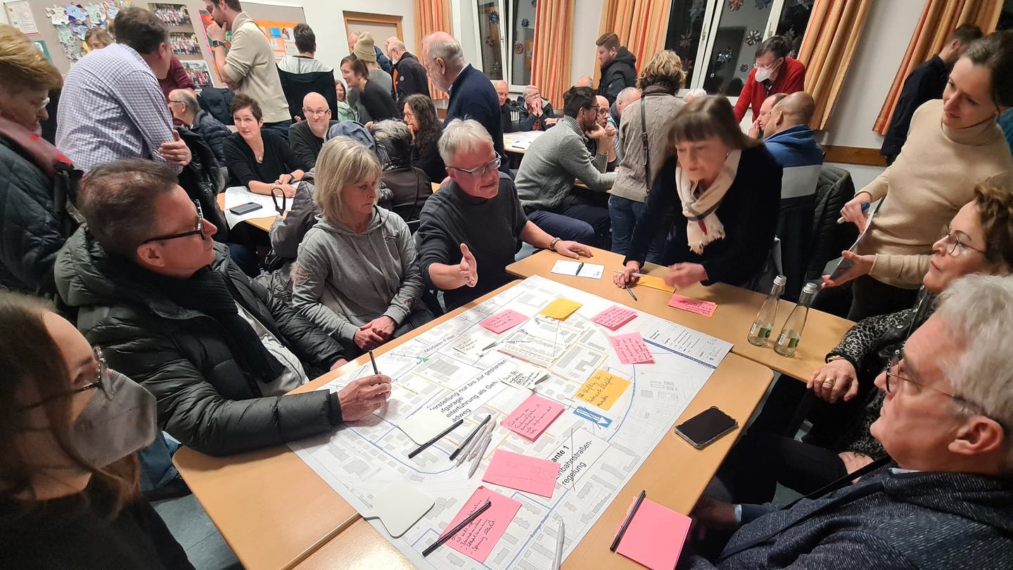 Bürgerinnen und Bürger sitzen um einen Tisch und beraten über ein Projekt in ihrer Stadt. In Mainz gibt es seit 2022 eine neue Form der Bürgerbeteiligung