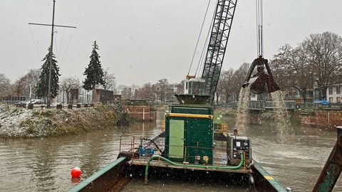 Ein Baggerschiff liegt im Dezember 2023 Winterhafen in Mainz und holt Schlamm vom Grund. Der Hafen muss ausgebaggert werden, damit im Sommer Sportboote bei Niedrigwasser nicht auf Grund laufen. 