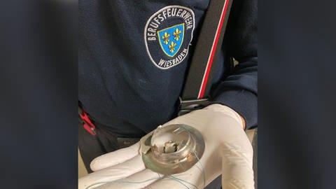 Das Abflussgitter in der Hand eines Feuerwehrmannes: Das Kind war in Wiesbaden mit den Fingern in dem Abfuss steckengeblieben