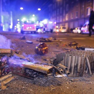 Abgebrannte Böller liegen nach der Silvesternacht auf der Straße, während im Hintergrund Einsatzkräfte der Feuerwehr stehen.