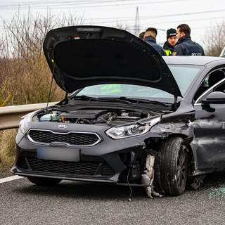 Eine stark beschädigtes Auto steht in der Autobahnabfahrt Hechtsheim-West. Dahinter stehen Polizisten.