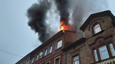 Aus dem Dachstuhl eines Mehrfamilienhauses kommen Flammen und Rauch.