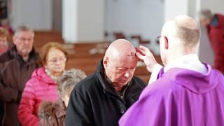 Pfarrer zeichnet Gemeindemitgliedern Aschekreuz auf die Stirn