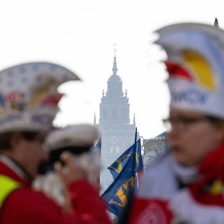 Mitglieder des Mainzer Carneval-Vereins stehen kurz vor Beginn des Rosenmontagsumzuges 2023 in Mainz in der Flucht mit dem Turm des Doms.