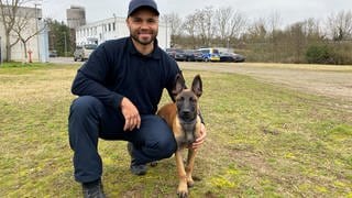 Der Polizist Maurice Schmitt kniet neben seinem Schäferhundewelpen und legt den Arm um den Hund.
