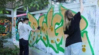 Zwei Jugendliche besprühen das alte Hallenbad in Oppenheim mit buntem Graffiti.